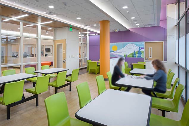 Dining room with playful, green seating and mural of mountains on back wall