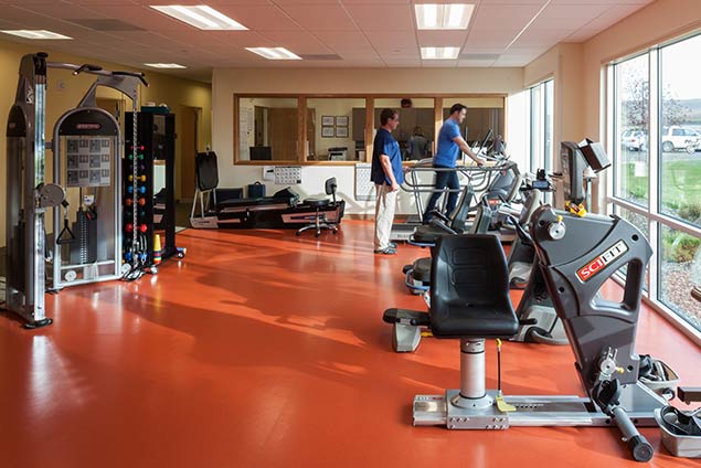 Gym with exercise equipment. Two people at the back working out