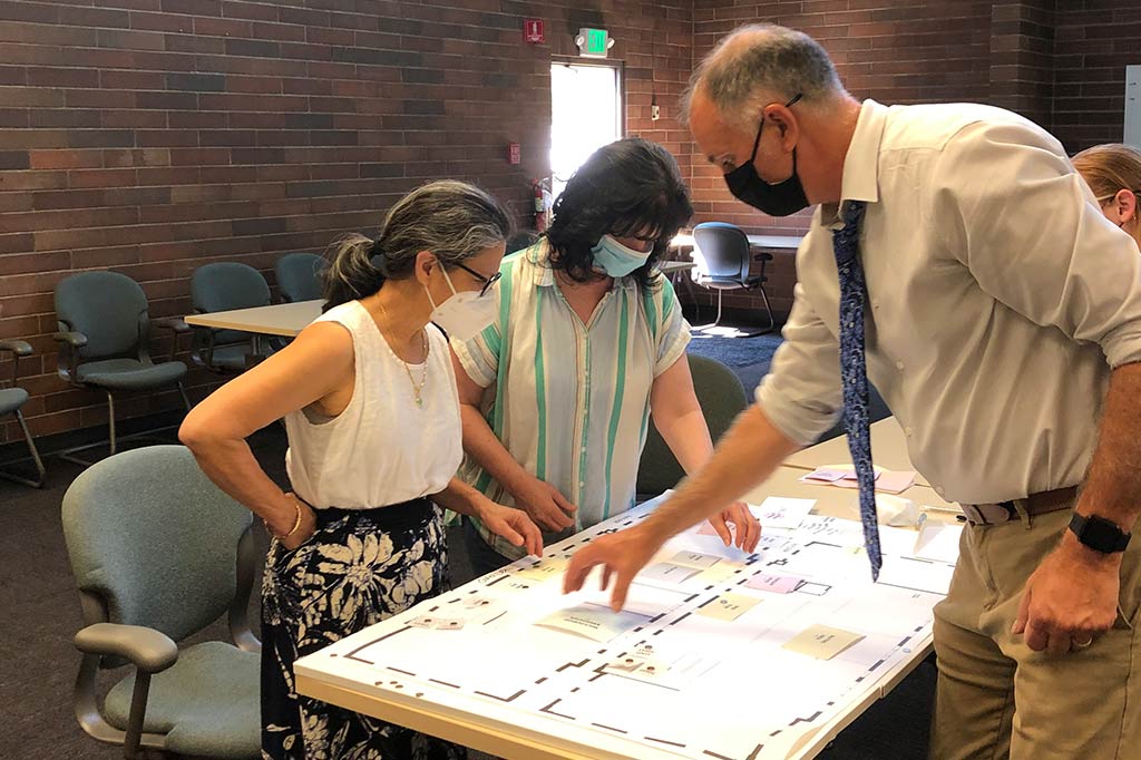 Two men and a woman standing at a table with architectural plans sitting on on it