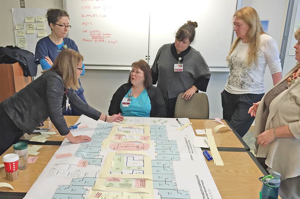 Six women standing at a table with architectural plans sitting on it.