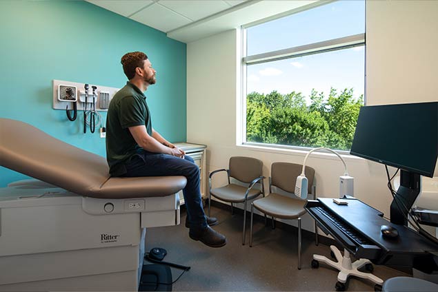 Man sitting on edge of hospital bed looking out window